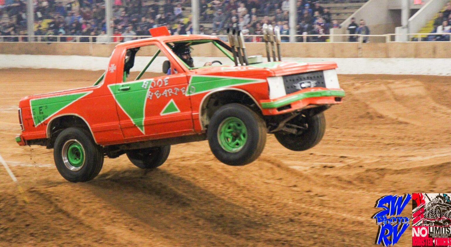 A red truck with green and white stripes is jumping over the dirt.